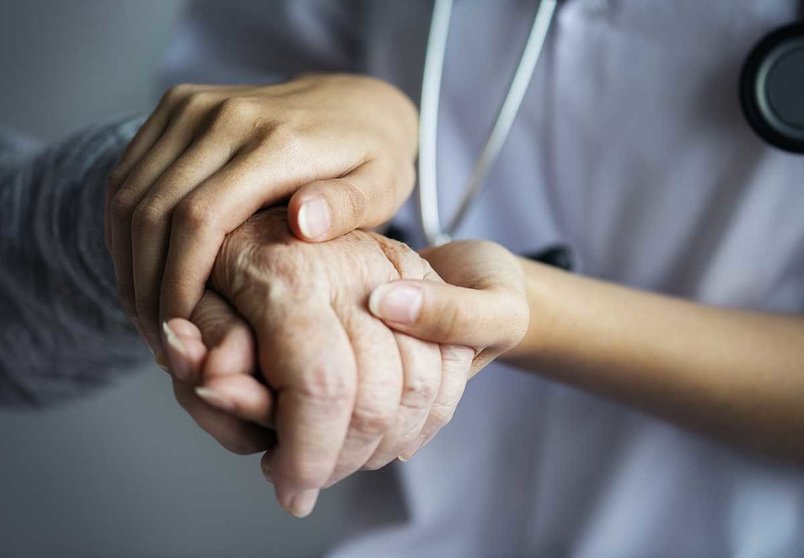 Una sanitaria acaricia la mano, curtida por la edad, de una anciana enferma.