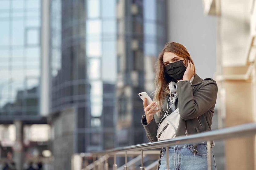Woman in the city. Person in a mask. Coronavirus theme. Girl walks with phone and headphones.