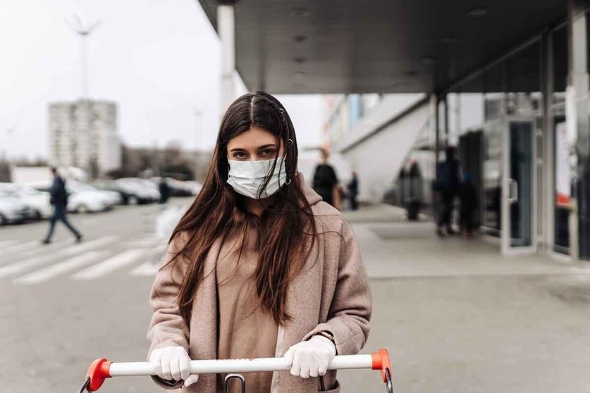 Young woman wearing protection face mask against coronavirus 2019-nCoV pushing a shopping cart. Concept of coronavirus