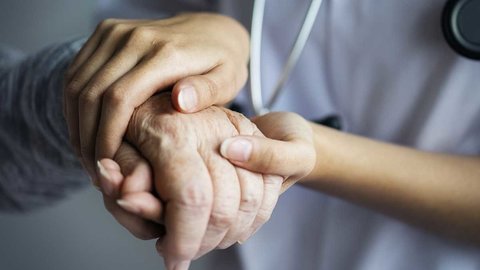 Una sanitaria acaricia la mano, curtida por la edad, de una anciana enferma.