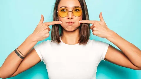 Young beautiful woman looking at camera.Trendy girl in casual summer white T-shirt and yellow skirt in round sunglasses. Positive female shows facial emotions.Funny model blowing her cheeks.Puff out