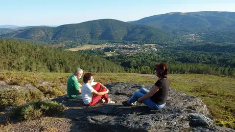 O rexedor lazano, Jes&uacute;s Blanco; a presidenta da Comunidade de Montes de Laza, Rosa L&oacute;pez, e a arque&oacute;loga Nieves Amado, sentadas no enclave recuperado cas vistas da vila &oacute; fondo.