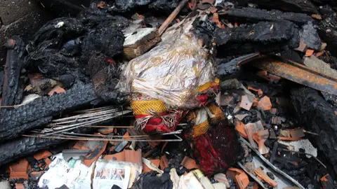 Unha chaqueta do traxe dun peliqueiro pequeno d&eacute;ixase entrever entre as trabes queimadas.
