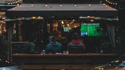 aficionados viendo un partido de f&uacute;tbol en un bar - yasin-alsbey-PE6A-Iytkks-unsplash