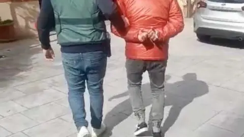 Un agente de la Guardia Civil traslada a uno de los detenidos en la operaci&oacute;n 'GULUX'.